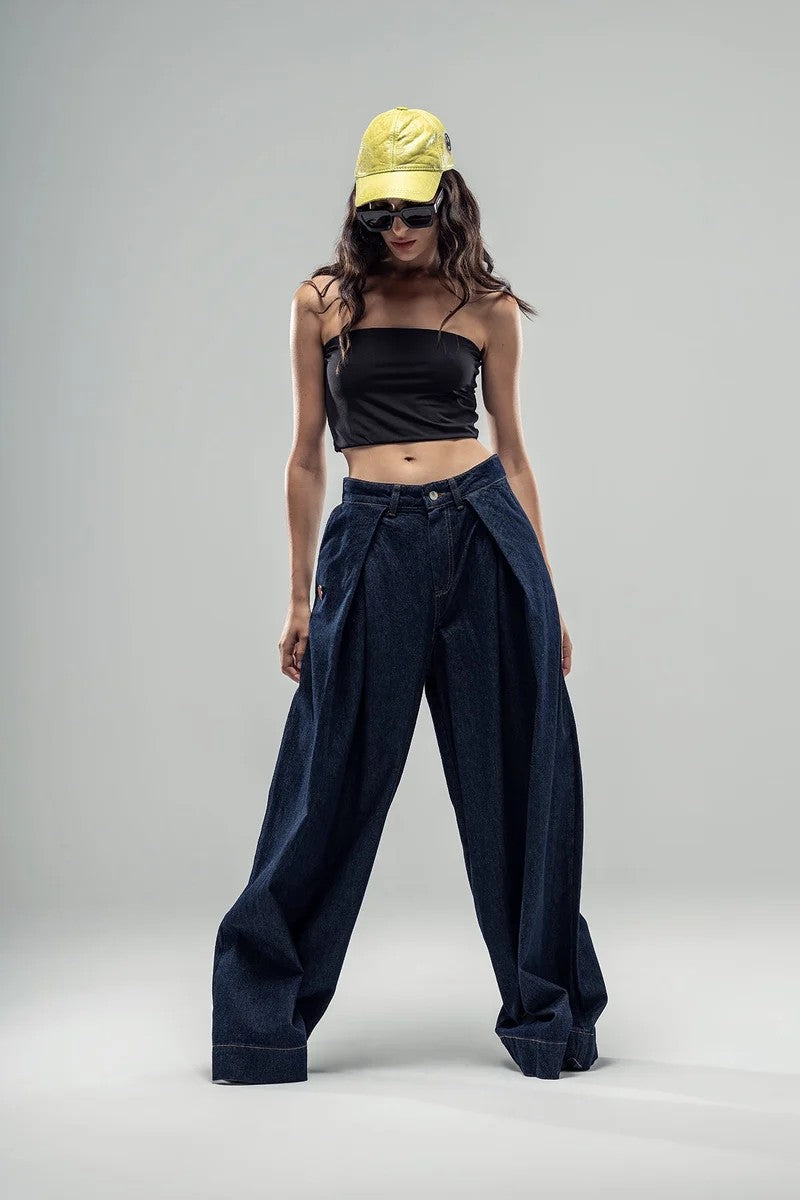 Look com top preto justo e calças largas em denim azul escuro com boné amarelo